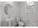 Bathroom features a pedestal sink, a round mirror, a toilet, and a window with natural light at 620 Altamonte Dr, Clover, SC 29710