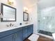 Bathroom with double sinks, blue cabinets, modern light fixtures, marble shower and a white tiled floor at 1012 Rockway Dr, Charlotte, NC 28205