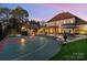 Rear view of the luxurious home with a swimming pool, cabana, and sports court at twilight at 3042 Kings Manor Dr, Weddington, NC 28104