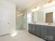 Bright bathroom with double vanity, gray cabinets, tile floors, and a glass enclosed shower at 3111 Vermillion Dr, Harrisburg, NC 28075