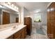 Well-lit bathroom featuring a large mirror, wooden cabinets, tub, and classic wallpaper at 16415 Capps Rd, Charlotte, NC 28278