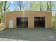 Spacious tan barn featuring two open bay doors, a single side door, and gravel driveway surrounded by trees at 10200 Amsterdam Dr, Mount Pleasant, NC 28124