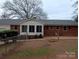 Exterior view of a brick home with a sunroom, patio, and a partially fenced yard with mature trees at 2044 Helen Dr, Gastonia, NC 28054