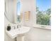 Contemporary powder room with pedestal sink, oval mirror, and window overlooking the trees at 2530 Park Rose Ln # 12, Charlotte, NC 28204