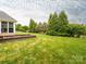 Spacious backyard with green lawn, garden beds, privacy trees, and a glimpse of the home's exterior at 3850 Hounslow Ln, Harrisburg, NC 28075