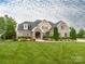 Charming brick home featuring a stone entryway, lush landscaping, and a well-manicured lawn at 3850 Hounslow Ln, Harrisburg, NC 28075