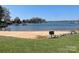 Scenic waterfront featuring a sandy beach, calm water, and lush green trees surrounding the beautiful lake at 16721 Spinnaker Ln, Cornelius, NC 28031