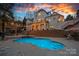 Beautiful backyard pool with a stone patio, string lights, outdoor seating, and lush landscaping for serene relaxation at 134 Wild Harbor Rd, Mooresville, NC 28117