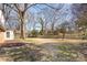 A large backyard with dormant grass, deciduous trees, and a view of an outbuilding on the side of the house at 821 Greentree Dr, Charlotte, NC 28211