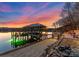 Beautiful covered boat dock featuring lighting, stone accents, and a serene waterfront setting at sunset at 296 Windemere Isle Rd, Statesville, NC 28677