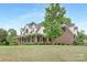 Expansive lawn and mature trees surround this two-story brick home with a welcoming front porch at 3300 Chancellor Ln, Monroe, NC 28110