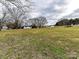 Wide shot of a one-story white home on a spacious lot with trees and storage building at 7514 Highway 205 Hwy, Marshville, NC 28103