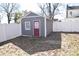 A gray shed with a red door sits on a leaf-strewn lot surrounded by a white fence at 604 Pearl Ave, Kannapolis, NC 28083