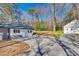 Charming home exterior with gravel driveway, white siding, black shutters, and a detached garage, set against a backdrop of mature trees at 2478 Stribling Cir, Lancaster, SC 29720