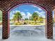 Framed view through a brick archway showcasing a serene lake and landscaped grounds with mature trees at 6823 Manatee Dr, Concord, NC 28025