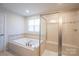 Bright bathroom features a tiled surround tub and glass-enclosed shower with a built-in seat at 10036 Paper Birch Dr, Charlotte, NC 28215