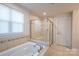 Bright bathroom features a tiled surround tub and glass-enclosed shower with a built-in seat at 10036 Paper Birch Dr, Charlotte, NC 28215