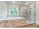 Bright bathroom with a window, tub and seamless glass-enclosed shower featuring marble style tiling and wood-look flooring at 3213 Mcharney Dr # 32, Harrisburg, NC 28075