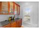 Wet bar featuring dark countertops, wood cabinets with glass doors, and a window for natural light at 4915 Ardenwoods Dr, Charlotte, NC 28215