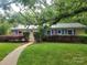 Charming single-story brick home with a metal roof, lush landscaping, and a walkway leading to the front door at 1552 10Th Street Nw Pl, Hickory, NC 28601