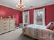 Cozy bedroom featuring bright red walls, wood dresser and a colorful chandelier at 9904 Duane Ct, Huntersville, NC 28078