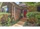 Close-up of a brick home featuring a red front door with detailed trim, complemented by lush landscaping at 12606 Bradford Hill Ln, Huntersville, NC 28078