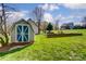 Backyard shed featuring double doors with an 'X' design, set against a backdrop of green grass and trees at 1207 Chadbourne Ave, Concord, NC 28027