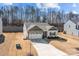 View of the home with driveway, lawn, and a wooded backdrop; exterior is gray with stone accents and dark trim at 127 Tradesmen Trl, Troutman, NC 28166