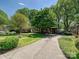 Beautiful landscaped front yard with mature trees, a long driveway, and a charming brick home in the background at 4132 Sulkirk Rd, Charlotte, NC 28210