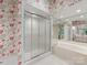 Bright bathroom featuring floral wallpaper, glass shower, and a large soaking tub with mirrored wall at 2027 Meadowood Ln, Charlotte, NC 28211