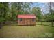 A storage shed situated in the backyard, featuring a wooden exterior, a red roof, and double doors at 124 Woodside Ln, Lancaster, SC 29720