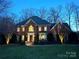 Stately brick home with mature landscaping illuminated at dusk, creating a warm and inviting curb appeal at 6301 Royal Aberdeen Ct, Charlotte, NC 28277
