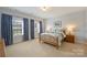 Bright bedroom features two windows with blue curtains, a wooden bed frame, and neutral carpeting at 100 Cliveden Ct, Belmont, NC 28012