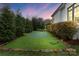 Backyard with a putting green, bordered with rock and shrubs, under a beautiful sunset sky at 4336 Tottenham Rd, Charlotte, NC 28226