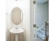 Elegant powder room with pedestal sink and decorative oval mirror, adjacent to carpeted stairs at 5337 Orchid Bloom Dr, Indian Land, SC 29707