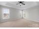 Bright bedroom featuring neutral carpeting, tray ceiling, fan, and ample natural light from multiple windows at 9413 Pastern Ct, Charlotte, NC 28216