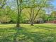 Spacious front lawn with mature trees surrounding a cozy one-story brick home and covered front porch at 6349 Lebanon Rd, Mint Hill, NC 28227