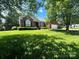 Charming brick home featuring lush green lawn and mature trees creating a serene curb appeal at 7700 Sedgebrook E Dr, Stanley, NC 28164