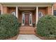 Inviting entryway with a classic wood door, brick steps, columns, and manicured bushes at 700 Queen Charlottes Ct, Charlotte, NC 28211
