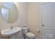 Well-lit half bathroom featuring a pedestal sink, white toilet, and a round mirror above the sink at 173 Glastonbury Dr, Mooresville, NC 28115