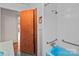 Bathroom with wood door, white tiled walls, and safety grab bars by a blue bathtub and shower at 136 Coble Ave, Albemarle, NC 28001