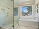 Bright bathroom features a glass shower, a modern tub near a large window, and tile flooring at 2004 Lombardy Cir, Charlotte, NC 28203