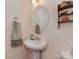 A half bathroom with a pedestal sink, oval mirror, decorative shelves, and a neutral color scheme provides a clean look at 4856 Pepper Dr, Harrisburg, NC 28075