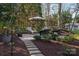 A serene backyard retreat featuring an outdoor lounge area with stone pathways, mature trees, and manicured landscaping at 107 Doris Ct, Lincolnton, NC 28092