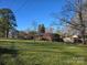 Expansive front yard view of a brick ranch-style home, featuring mature trees and lush green grass, inviting relaxation at 624 Patricia Ave, Harrisburg, NC 28075
