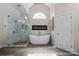Elegant bathroom featuring a glass-enclosed shower, soaking tub, fireplace, and large arched window at 9433 Wallace Pond Dr, Huntersville, NC 28078