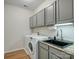 Well-lit laundry room featuring a washer, dryer, sink, and gray cabinets for ample storage at 1033 Ridge Haven Rd, Waxhaw, NC 28173