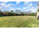Expansive backyard featuring a lush green lawn, mature trees, and a brick home under a bright blue sky at 8137 Caliterra Dr, Charlotte, NC 28227