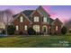 Charming two-story brick home with meticulously manicured lawn and mature landscaping at twilight at 8018 Cotton St, Harrisburg, NC 28075