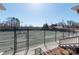 View of a well-maintained tennis court surrounded by a tall fence, trees, and lush greenery at 9036 Saint Thomas Ln, Charlotte, NC 28277